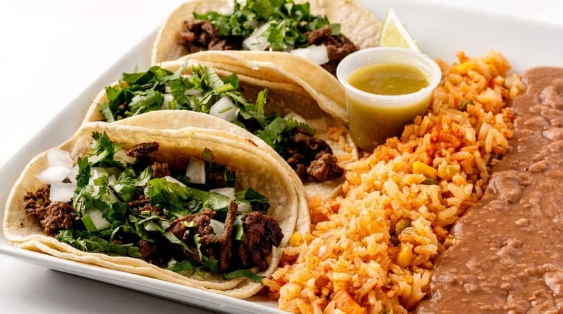 Three beef tacos with cilantro and onions, served with rice, refried beans, and salsa.